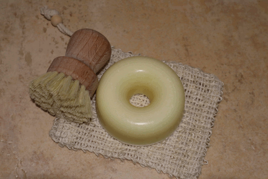Dies ist ein Foto von runden Spülseife der Firma Reinland Seifen und eine Spülbürste auf einem Seifensäckchen